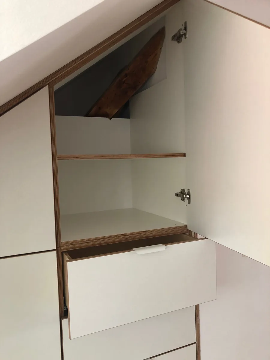 Oberer Teil des Einbaus, geöffnet: ein Regalfach unter dem alten Dachbalken, der sichtbar bleibt, darunter ein herausgezogener Schubkasten.