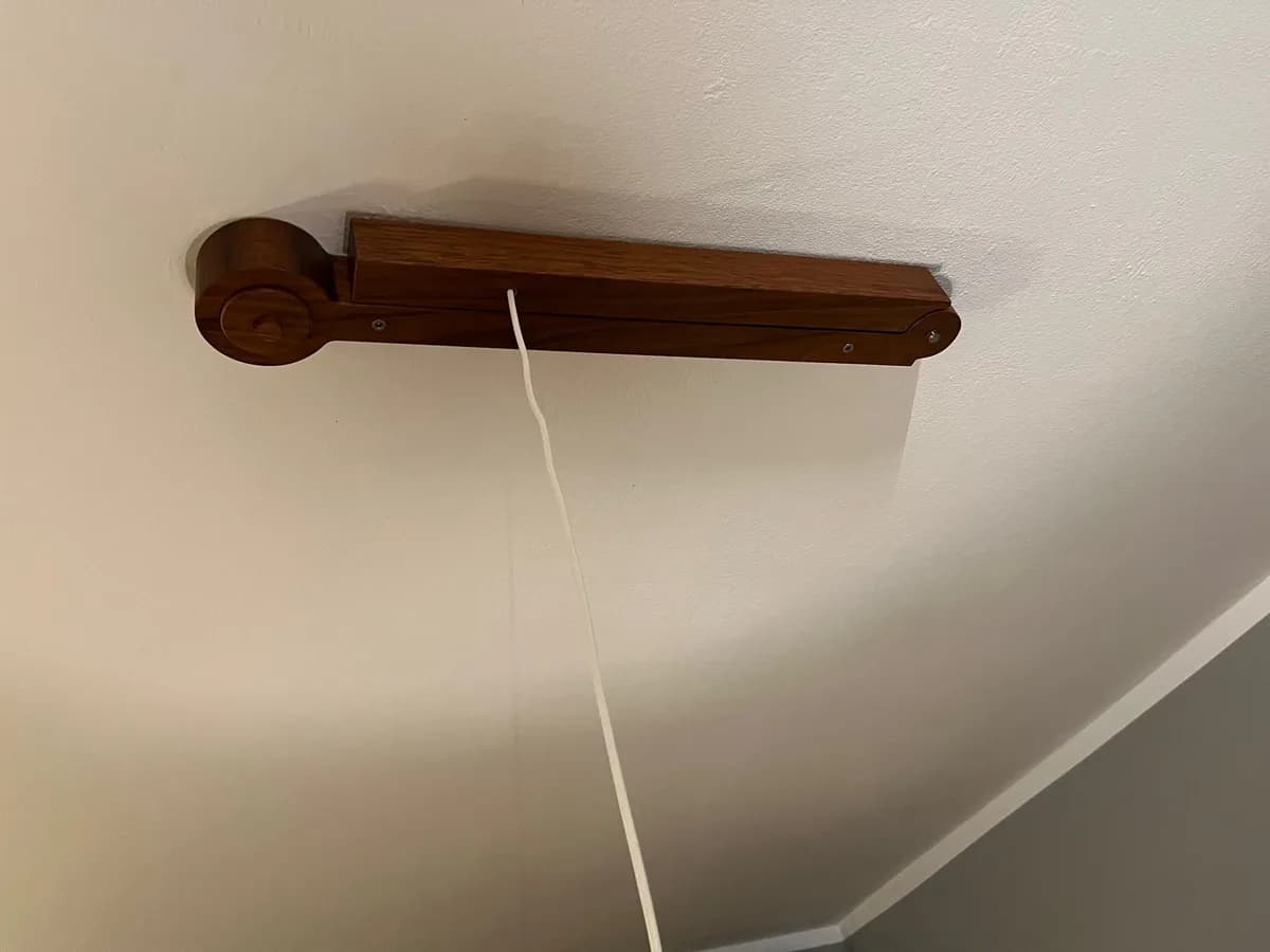 The jatoba lamp arm folded together against the ceiling: the two sections lie on each other, the round joint at one end, the white cable hanging down.