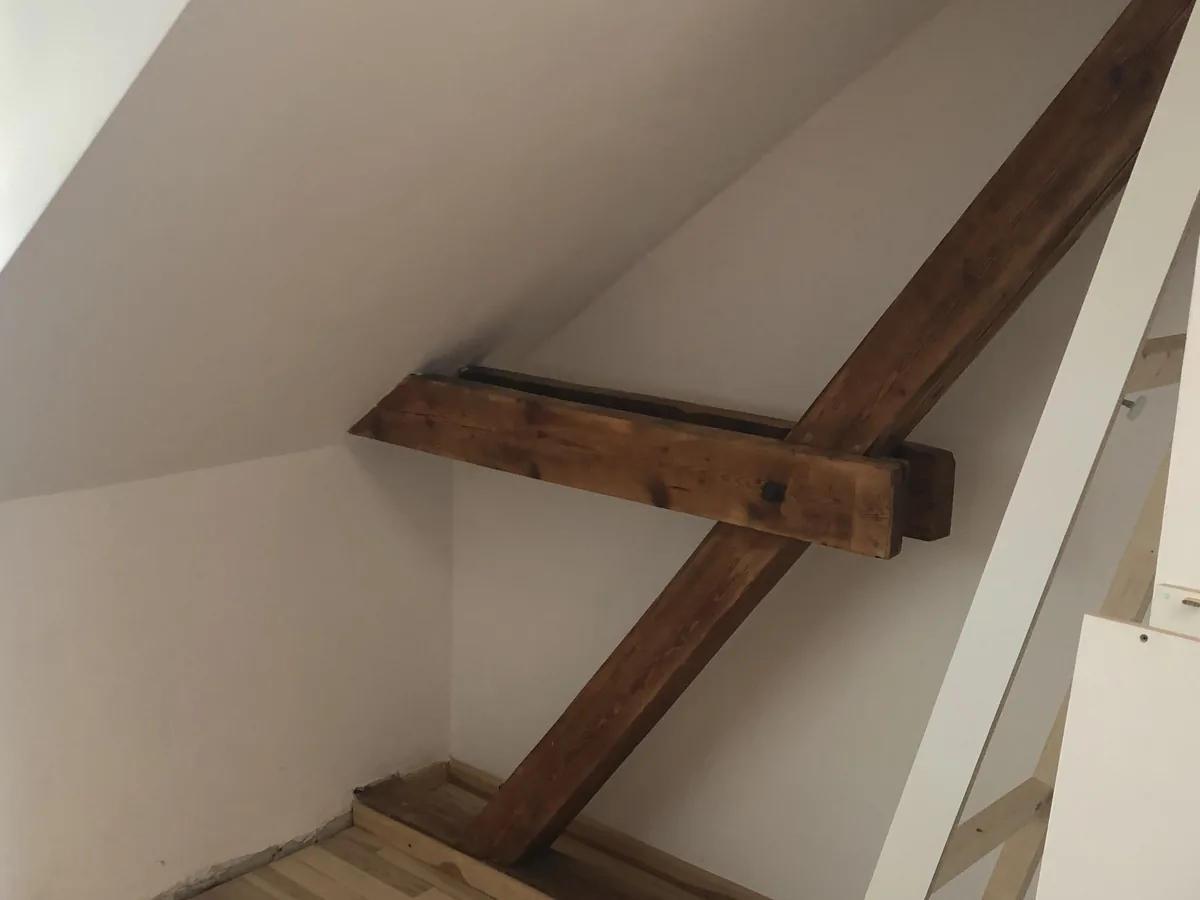 Derselbe Dachraum in der Hufeisensiedlung vor dem Einbau: freiliegende Sparren und Kehlbalken unter der Schräge, Wände verputzt, Boden bereits verlegt.
