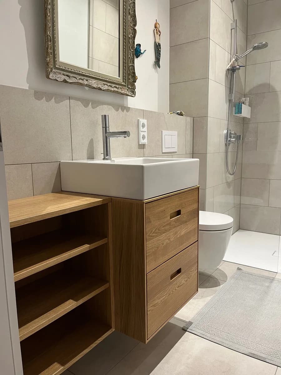 Oak washstand mounted off the wall, with two drawers and milled finger pulls. An open shelf section sits lower to the left, with the WC and a level-access shower behind.