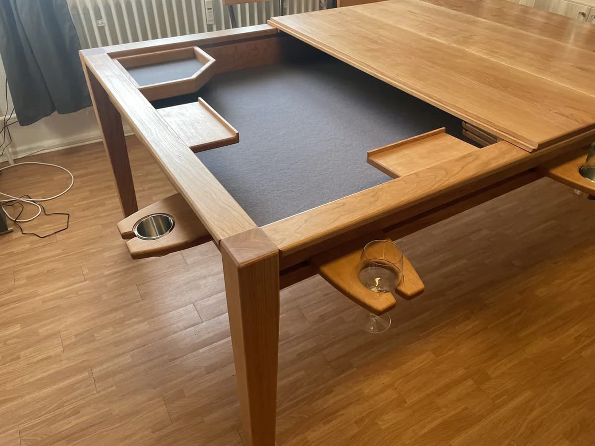 The games table with the panels half in place: on the right the solid wood panel covers the playing surface, on the left the grey felt stays open. A five-sided dice tray, two rectangular trays and, on the outside, two glass holders with a glass and a cup hook into the grooves along the edge.