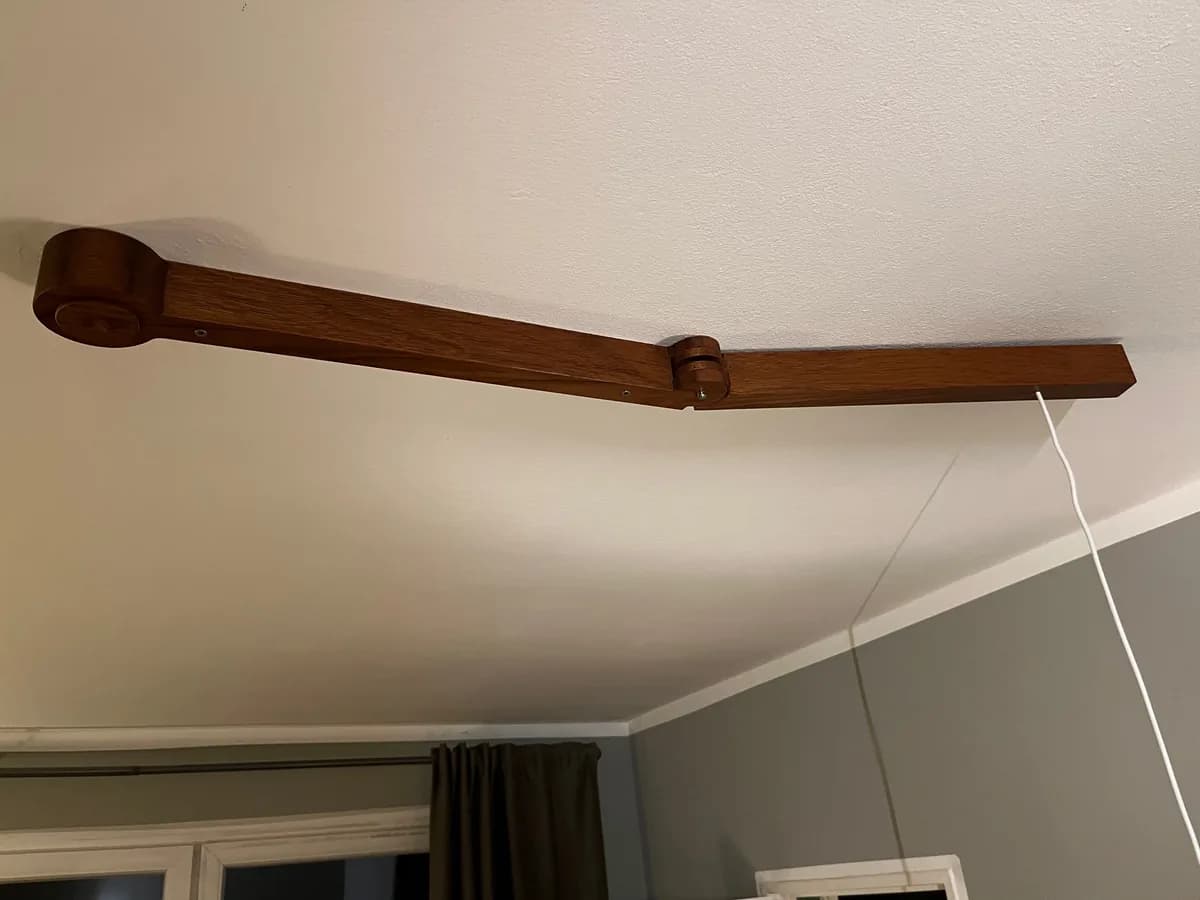 Zweiteiliger Lampenarm aus dunkel geöltem Jatoba, an der Decke montiert, mit einem Gelenk in der Mitte. Am freien Ende hängt das Kabel für die Lampe.