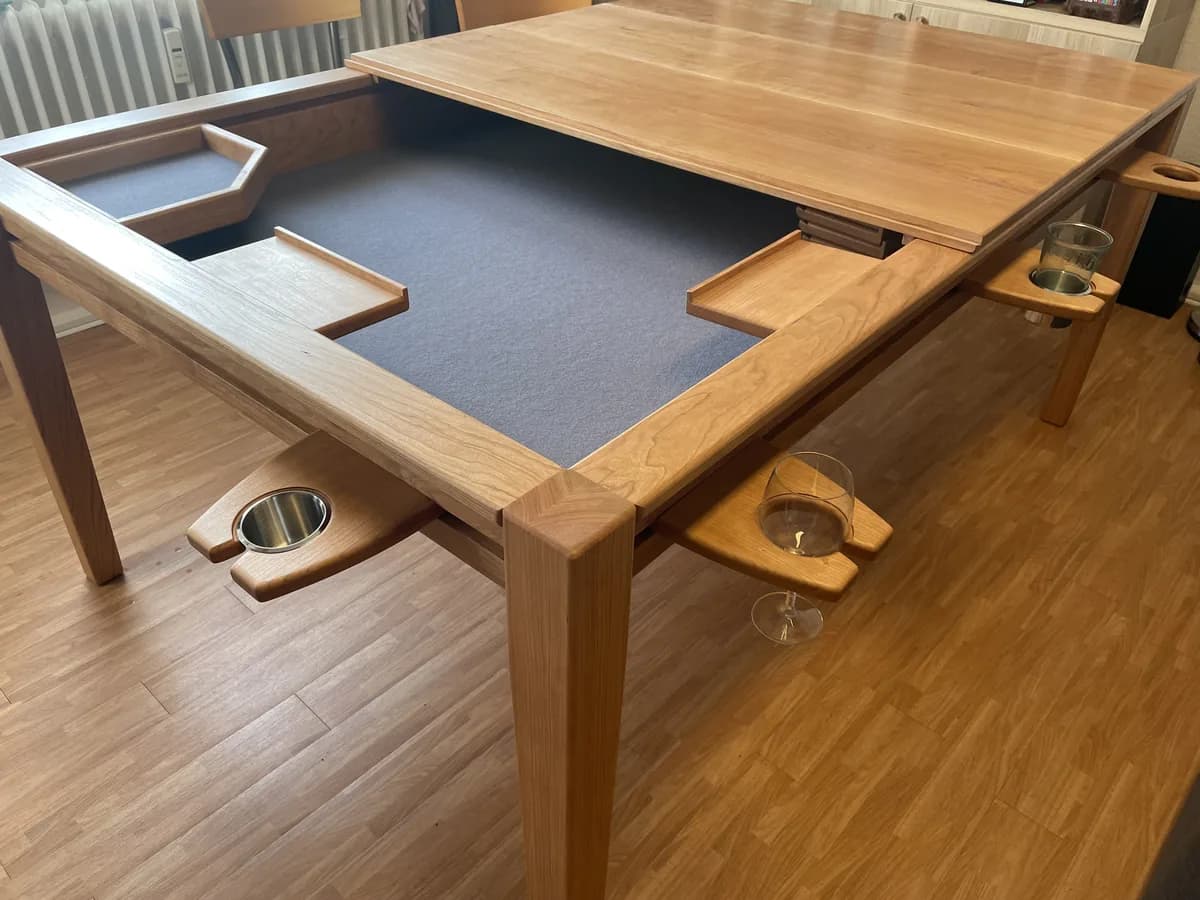 Spieltisch aus Kirschbaum: die vertiefte Spielfläche mit dunkelgrauem Filz, zur Hälfte von einer aufgelegten Massivholzplatte bedeckt. An den Rändern eingehängte Glashalter mit Gläsern und mehrere Ablageschalen.