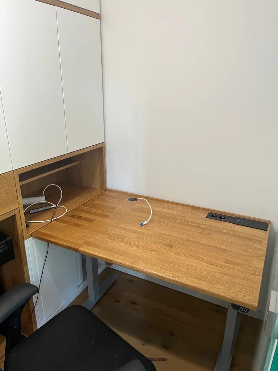 Solid oak desktop on a height-adjustable frame, with sockets recessed into the edge and the open cable-routing compartment above it.