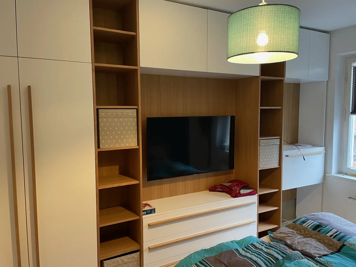 The opposite wall: television recess with a oak back panel, a lowboard with three drawers beneath, open shelving towers left and right, closed compartments above; the writing desk by the window on the right.