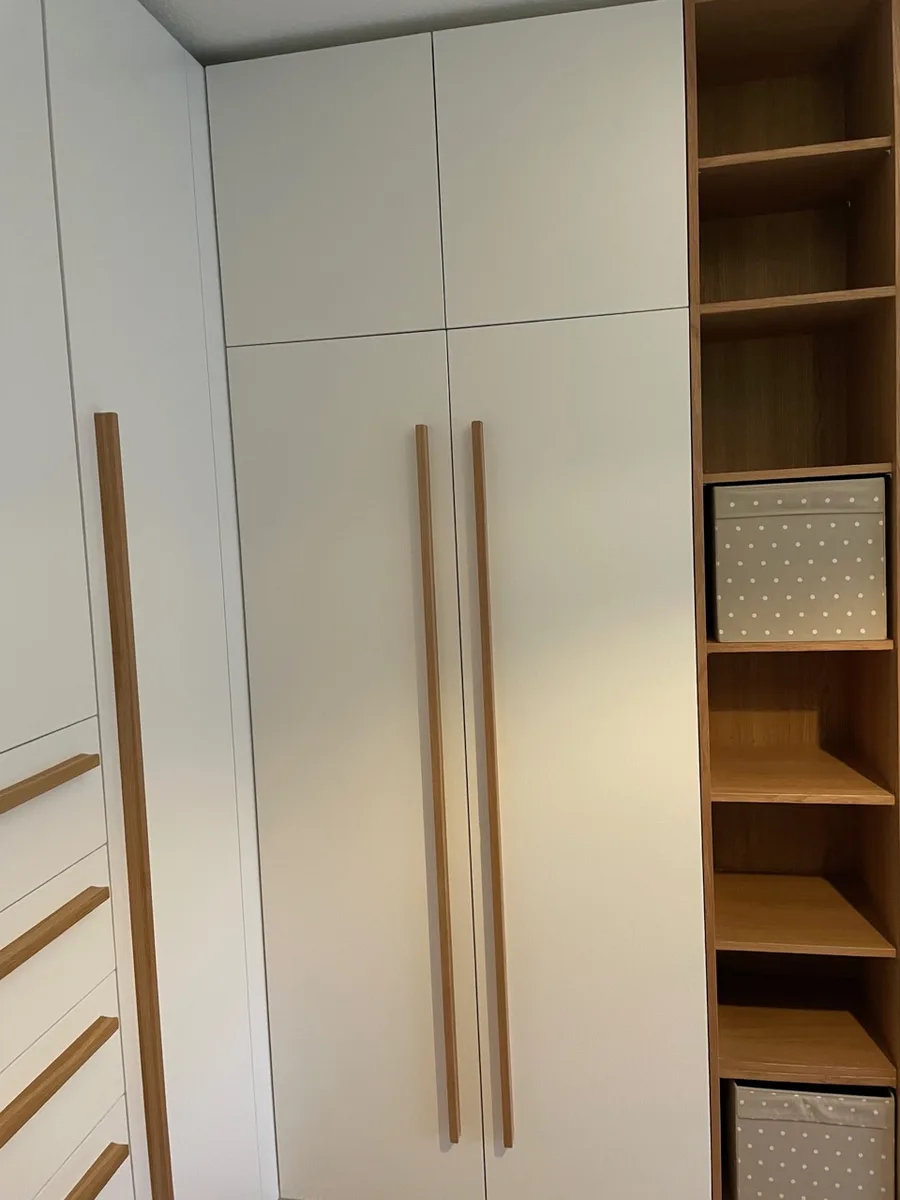 Close-up of the wardrobe doors: two long handle rails in oak, the drawers with their rails on the left, the open shelving tower with fabric boxes on the right.
