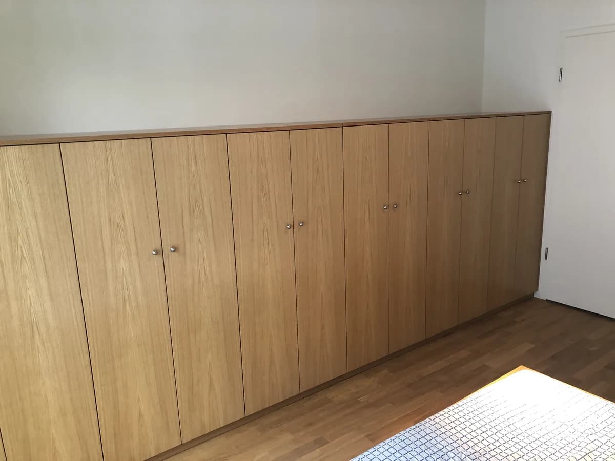 The cupboard runs the whole length of the wall, its oak-veneered fronts carrying small round knobs, the veneer figure running on across the doors.